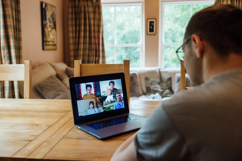 A young man speaking to others on a Zoom call. You can see the other group participants on the laptop screen.