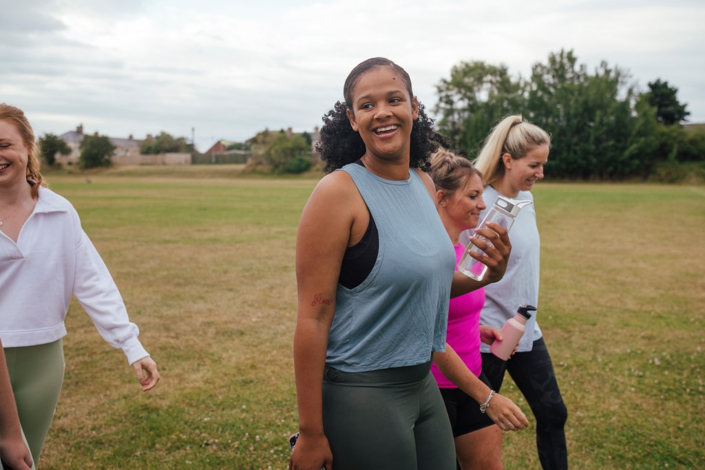 A side-view shot of a group of female friends walking outdoors on a field. They all smile widely.