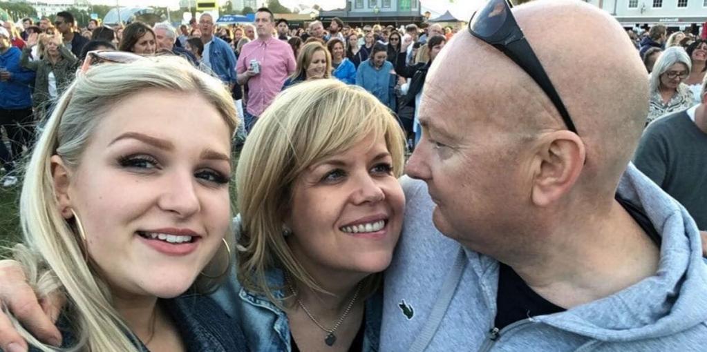 A photo of Rich with his wife and daughter taking a selfie in a crowd of people.