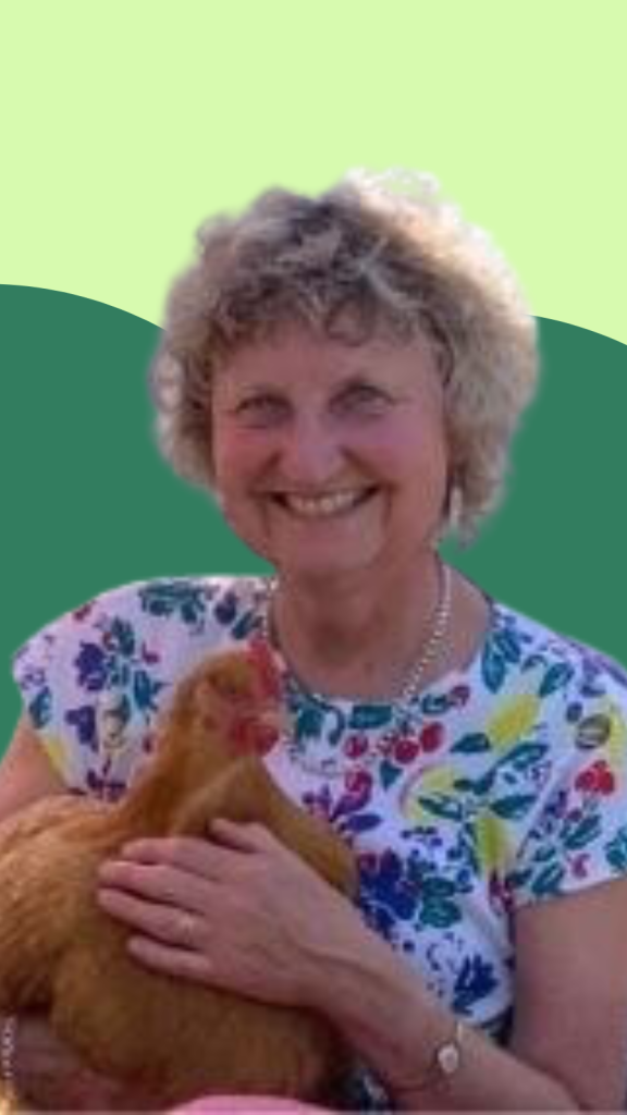 A photo of Victoria, a white woman with curly short hair. She is holding a chicken in her lap!