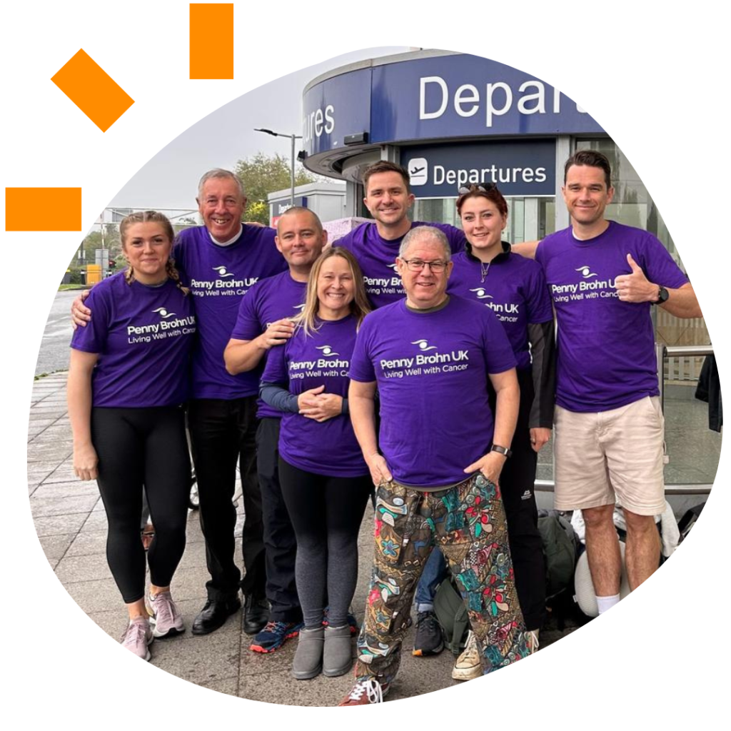 Group of people, 3 women and 5 men, wearing purple tshirts standing outside a departures gate at an airport.