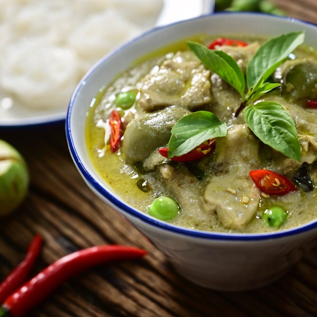 A bowl of Thai green curry with a bowl of rice in the background