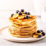 A picture of a plate of pancakes with blueberries and bananas on