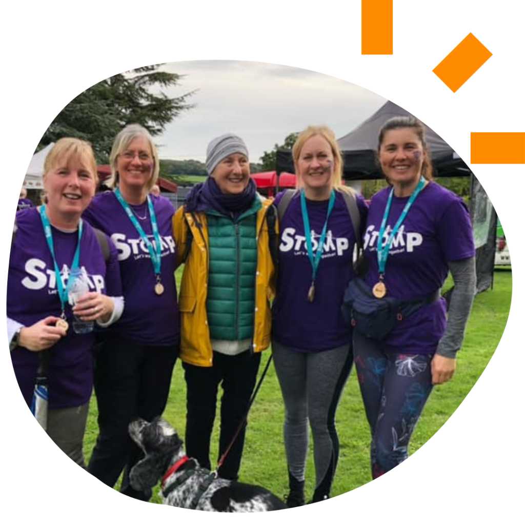 Photo of a group of 5 women wearing purple Stomp t-shirts and medals having just completed a walking challenge.