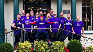Group of individuals standing infront of a hotel door wearing purple Penny Brohn UK tshirts.
