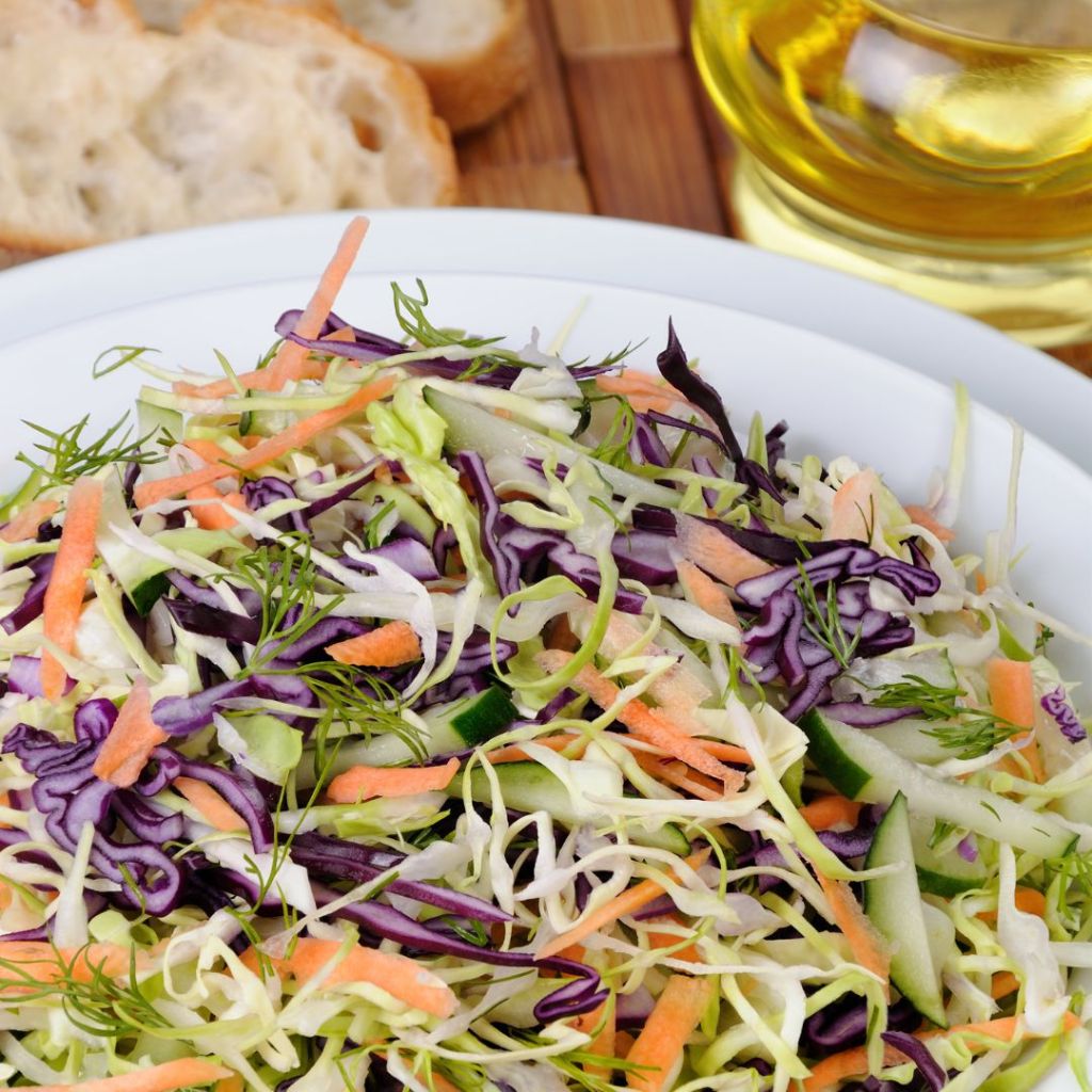 A bowl of coleslaw with a jug of oil in the background