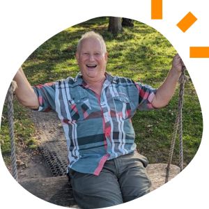 Robert, 60s, wearing a checkered shirt, smiling, sitting on a swing.