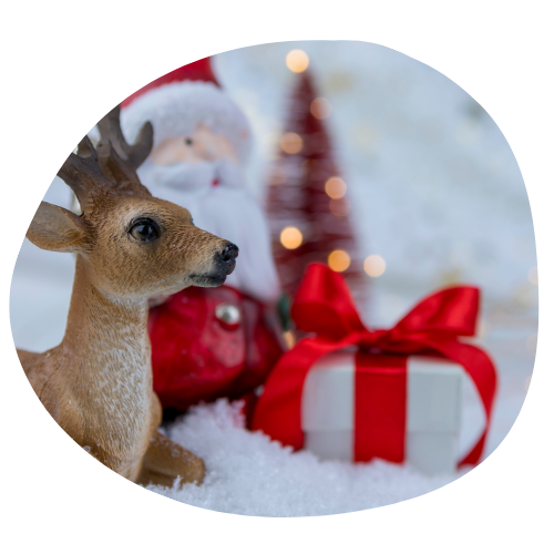 Photo of a reindeer on a snowy landscape with a blurred Christmas tree in the background.