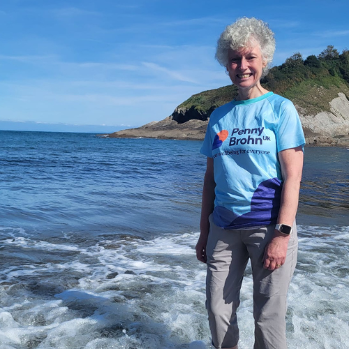 Sue Lloyd wearing a Penny Brohn UK t-shirt standing in the sea.