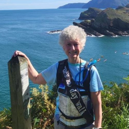 Sue Lloyd standing next to a marker with the sea behind her.