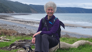 Sue Lloyd sat on a piece of driftwood with the sea behind her.