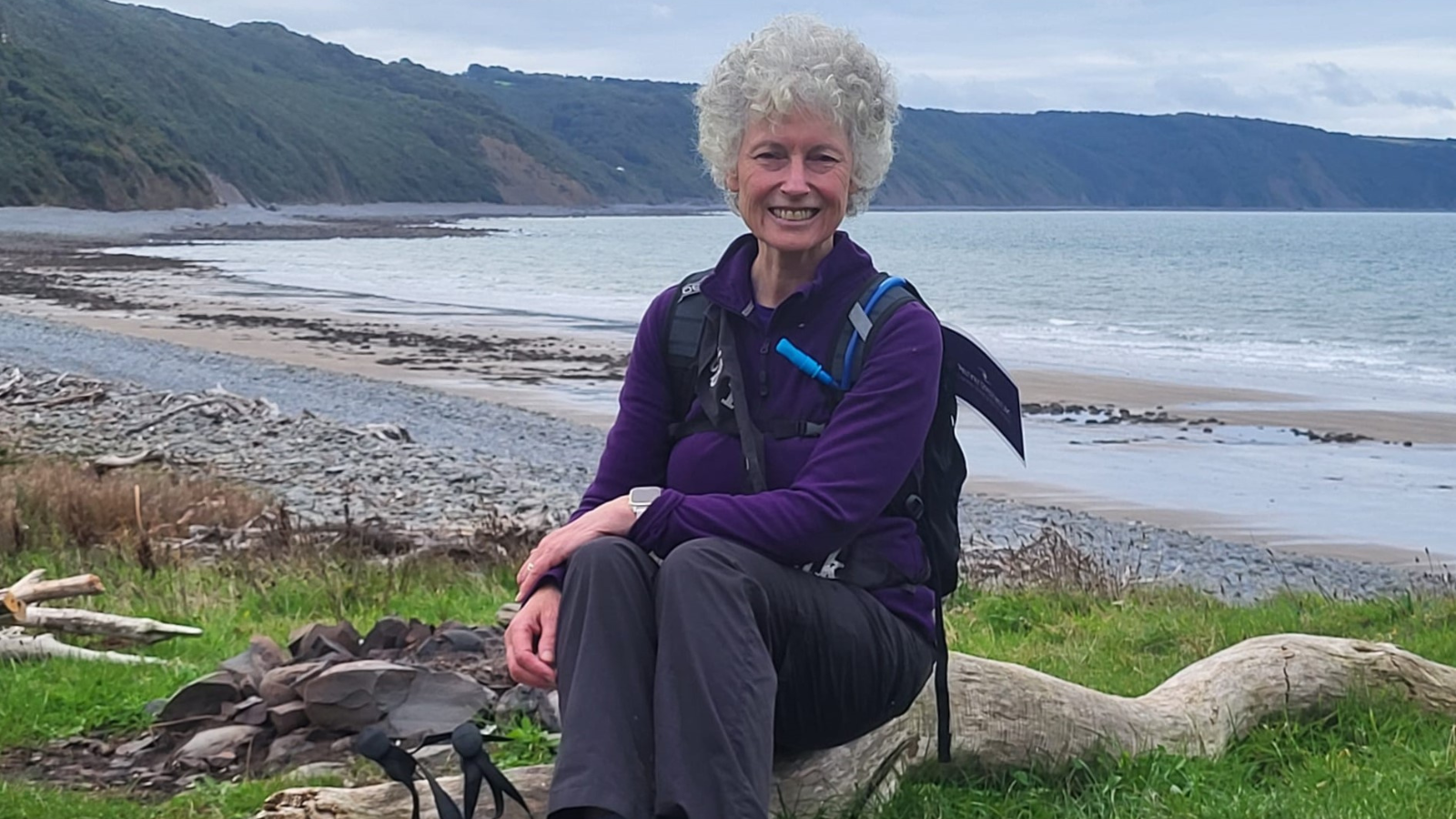 Sue Lloyd sat on a piece of driftwood with the sea behind her.
